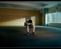 An image of a prisoner, in a film, in a wide open space, sat in the middle of the room, their head bowed sorrowfully. 