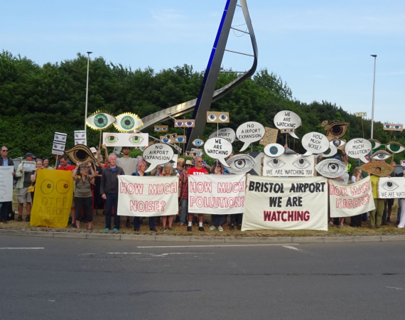 Grounding technologies funded team Eyes on Bristol Airport staging a protest outside Bristol Airport with signs that look like eyes